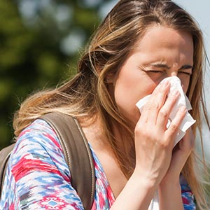 Woman on couch with nasal congestion under blanket blowing nose into tissue